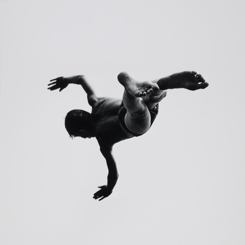 Black-and-white photograph by Aaron Siskind: a diver seen from below, suspended against a white sky, arms and legs thrown outward.
